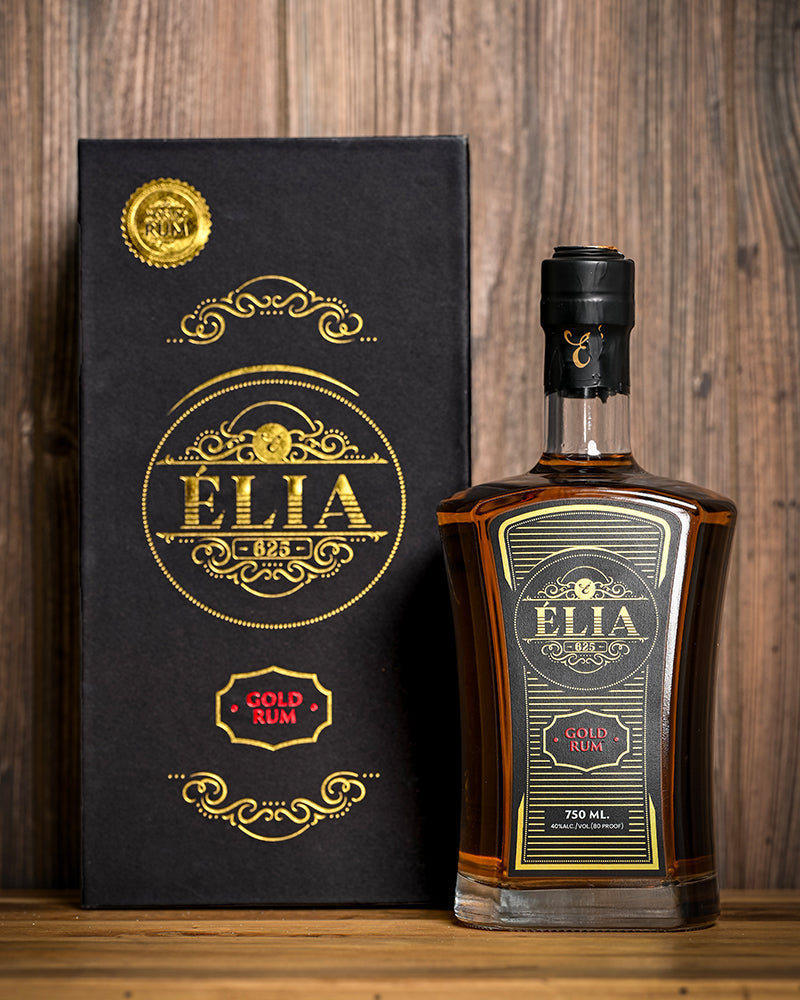 Élia625 Gold Rum in its presentation box, photographed against warm wood